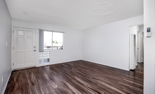 A room with a white door and a window with a view of a balcony.